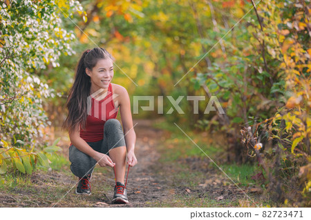 Autumn outdoor exercise lifestyle. Asian runner woman tying running shoes ready to run for fitness cardio workout in forest nature Autumn outdoor exercise lifestyle. Asian runner woman tying running shoes ready to run for fitness cardio workout in forest nature 82723471