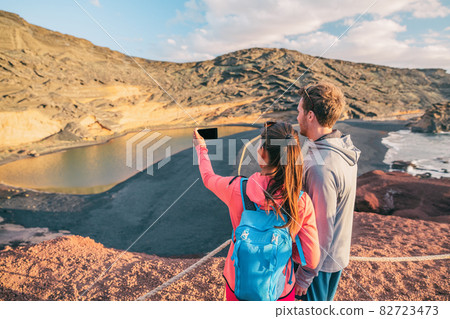 Hikers taking phone photo hiking in Spain mountain landscape . Travel couple tourists on summer hike with backpack. Woman, caucasian man hikers happy in Lanzarote National Park, Spain, Europe Hikers taking phone photo hiking in Spain mountain landscape . Travel couple tourists on summer hike with backpack. Woman, caucasian man hikers happy in Lanzarote National Park, Spain, Europe 82723473