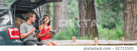 Road trip couple tourist eating food lunch at back of car on summer camping vacation travel. Happy driving people Road trip couple tourist eating food lunch at back of car on summer camping vacation travel. Happy driving people 82723505