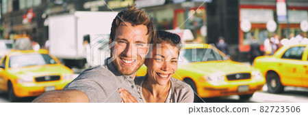 New York selfie couple taking photo on NYC city summer holiday vacation travel with yellow taxi cabs panoramic background. Man and woman tourists happy smiling 82723506