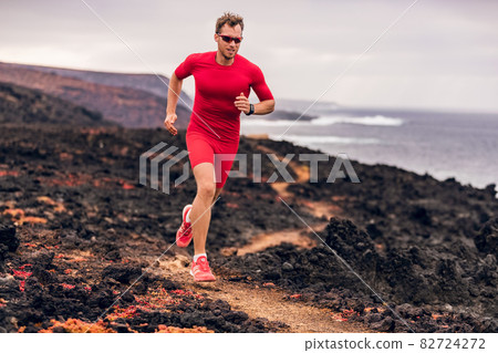 Mountain running ultra runner man athlete training cardio outdoor in extreme conditions on volcanic trail in coast landscape. Wet red rocks. Sports athlete wearing compression clothes and shoes Mountain running ultra runner man athlete training cardio outdoor in extreme conditions on volcanic trail in coast landscape. Wet red rocks. Sports athlete wearing compression clothes and shoes 82724272
