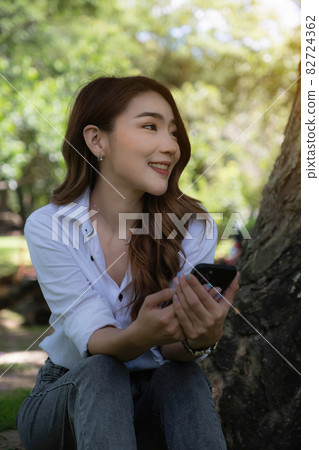 Portrait of Asian beautiful woman using smartphone at outdoor park. 82724362