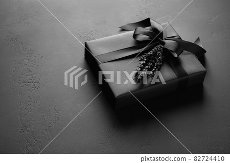 Festive black gift wrapped in paper with ribbon on black surface. 82724410