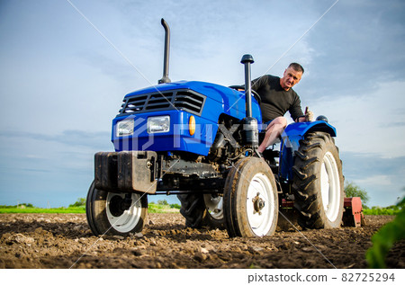 A farmer on a tractor cleans the field after harvest. Preparation of land for future planting new crop. Intensive land use. Milling soil, loosening ground before cutting rows. Farming, agriculture. A farmer on a tractor cleans the field after harvest. Preparation of land for future planting new crop. Intensive land use. Milling soil, loosening ground before cutting rows. Farming, agriculture. 82725294