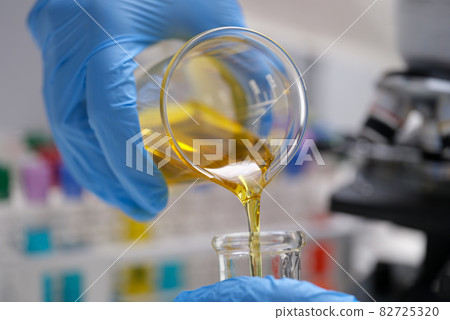 Chemist pouring edible oil from flask into test tube closeup Chemist pouring edible oil from flask into test tube closeup 82725320