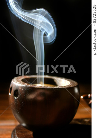 A thin trail of smoke rises from a brown cup-like incense holder 82725529