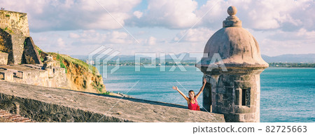 San Juan Puerto Rico travel happy tourist woman waving open arms in happiness at watch tower of Castillo San Felipe del Morro panoramic banner background 82725663