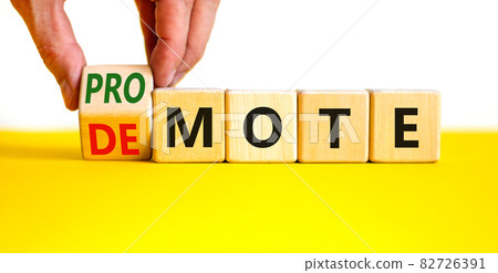 Promote or demote symbol. Businessman turns a cube and changes the word 'demote' to 'promote'. Beautiful yellow table, white background. Business, demote or promote concept. Copy space. Promote or demote symbol. Businessman turns a cube and changes the word 'demote' to 'promote'. Beautiful yellow table, white background. Business, demote or promote concept. Copy space. 82726391