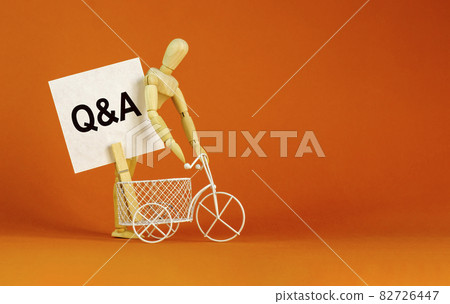 Questions and answers symbol. White paper. Words 'Q and A, Questions and answers'. Miniature bicycle, wooden human. Beautiful orange background. Business and Q and A concept, copy space. 82726447