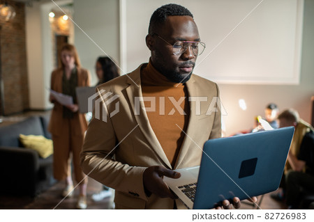 Young serious businessman looking at screen of laptop in his hands 82726983