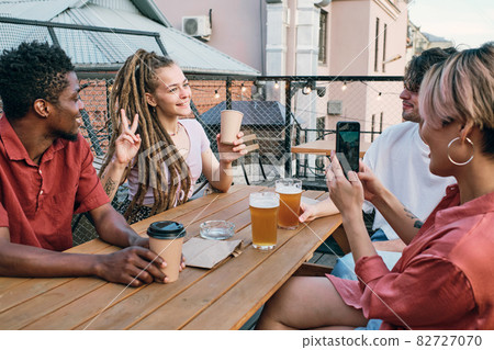 Happy girl with drink posing for camera of her friend with smartphone Happy girl with drink posing for camera of her friend with smartphone 82727070