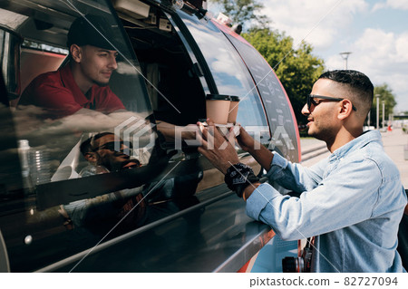 Guy in casualwear and sunglasses buying two drinks in food truck Guy in casualwear and sunglasses buying two drinks in food truck 82727094