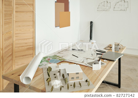 Wooden table with paper house models, sketches and mobile gadgets 82727142