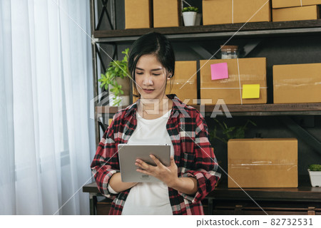 Asian woman startup small business at home office. Online seller entrepreneur young asian woman use tablet checking online order. Woman using tablet check stock goods supply delivery package shipping 82732531