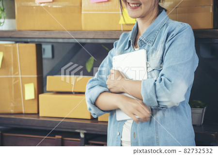 Asian woman startup small business at home office. Online seller entrepreneur young asian woman use tablet checking online order. Woman using tablet check stock goods supply delivery package shipping 82732532