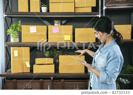 Asian woman startup small business at home office. Online seller entrepreneur young asian woman use tablet checking online order. Woman using tablet check stock goods supply delivery package shipping 82732533
