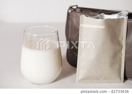 collagen powder travel pack and a glass of milk to make protein cocktail. collagen peptides powder for healthy drink. support for beautiful skin. lady's bag to take a protein sachet to go 82733636