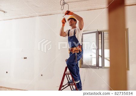 Smiling electrician fixing electric cable on ceiling 82735034