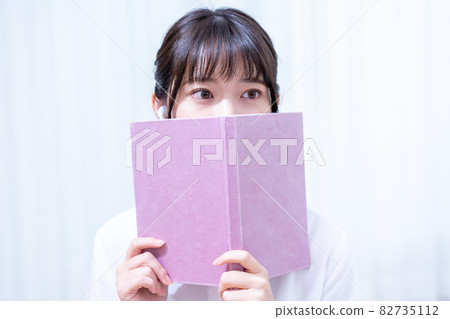 A young woman hiding her face in a book 82735112