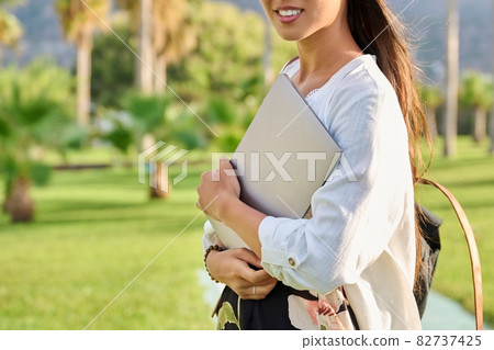 Outdoor portrait of young woman with laptop and backpack. 82737425