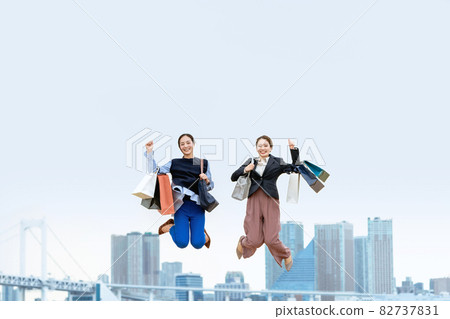 Two women jumping with a lot of shopping bags (sale / explosive buying) 82737831