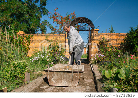 Eldery man kneads cement for pouring a garden path, garden construction work Eldery man kneads cement for pouring a garden path, garden construction work 82738639