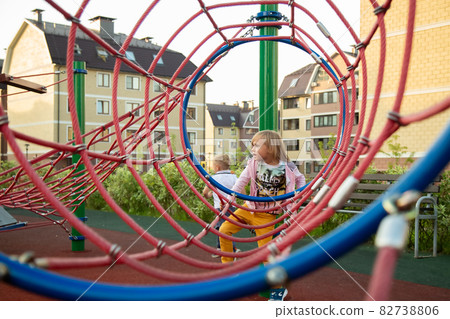 The little girl climbs ropes at the playground The little girl climbs ropes at the playground 82738806