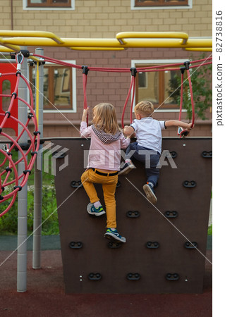 Caucasian boy and a girl climb the climbing wall in the playground Caucasian boy and a girl climb the climbing wall in the playground 82738816