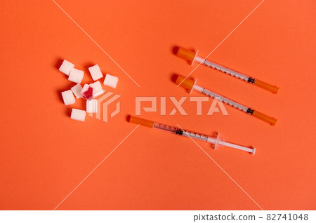 Flat lay composition of insulin syringes and white sugar cubes with blood drop isolated over colored orange background with copy space for medical ad. World diabetes day awareness concept, 14 November Flat lay composition of insulin syringes and white sugar cubes with blood drop isolated over colored orange background with copy space for medical ad. World diabetes day awareness concept, 14 November 82741048