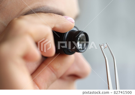 Woman looks through magnifying glass at precious stone 82741500