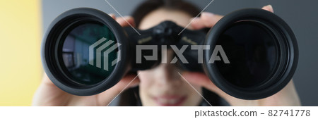 Young woman looking through black professional binoculars closeup 82741778