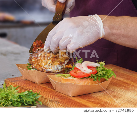 A chef prepares a burger for a customer. A man wearing white protective gloves picks up the burgers from the grill and and adds them to the burger bun. A chef prepares a burger for a customer. A man wearing white protective gloves picks up the burgers from the grill and and adds them to the burger bun. 82741990