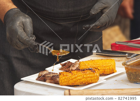 Chef prepares paper trays with grilled food, meat and corn for customers Chef prepares paper trays with grilled food, meat and corn for customers 82741995