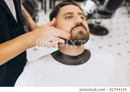 Professional barber, clipper cutting, shaving beard of regular customer at barbershop. Beauty, selfcare, style, fashion and male cosmetics concept. Professional barber, clipper cutting, shaving beard of regular customer at barbershop. Beauty, selfcare, style, fashion and male cosmetics concept. 82744145