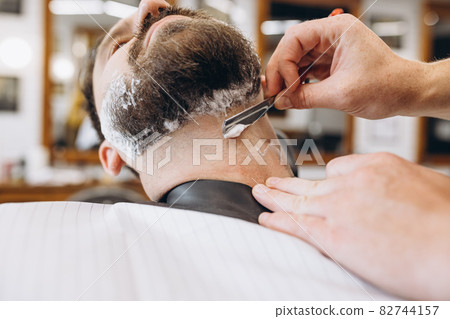 Man getting haircut at the barbershop. Professional barber at work process. Beauty, selfcare, style, fashion, healthcare and male cosmetics concept. Man getting haircut at the barbershop. Professional barber at work process. Beauty, selfcare, style, fashion, healthcare and male cosmetics concept. 82744157