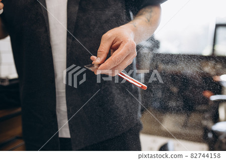 Close-up male hands of barber, clipper with professional tools at barbershop. Beauty, selfcare, style, fashion and male cosmetics concept. Close-up male hands of barber, clipper with professional tools at barbershop. Beauty, selfcare, style, fashion and male cosmetics concept. 82744158