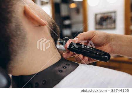 Close-up male hands with safety razor shave beard of customer at barbershop. Beauty, selfcare, style, fashion and male cosmetics concept. Close-up male hands with safety razor shave beard of customer at barbershop. Beauty, selfcare, style, fashion and male cosmetics concept. 82744196