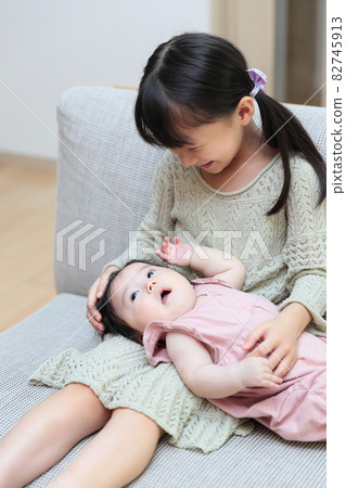 Baby and toddler close sisters sitting on the couch Baby and toddler close sisters sitting on the couch 82745913
