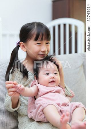 嬰兒和蹣跚學步的親密姐妹坐在沙發上 嬰兒和蹣跚學步的親密姐妹坐在沙發上 82745914