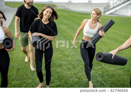 People walking with fitness mats on green meadow People walking with fitness mats on green meadow 82746698
