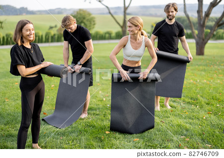 People fold fitness mats after training on meadow 82746709