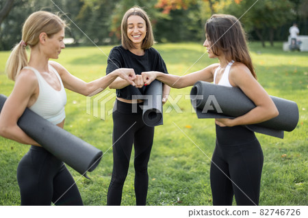 Girls with fitness mats bumping fists on meadow Girls with fitness mats bumping fists on meadow 82746726