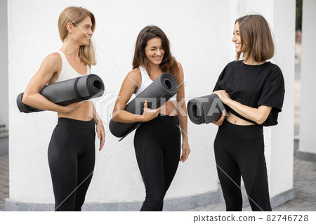 Girls stand with fitness mats and talk outdoors 82746728