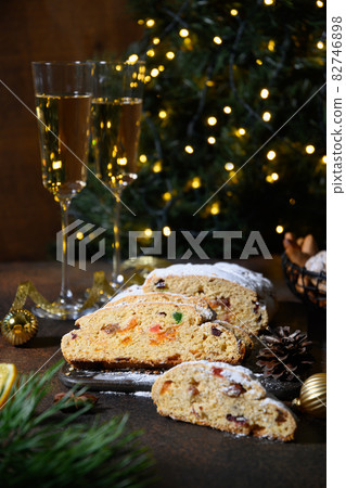 Traditional stollen decorated holiday rope on dark festive table with Christmas tree. Traditional stollen decorated holiday rope on dark festive table with Christmas tree. 82746898