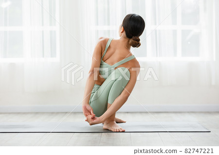Side view of Asian woman wearing green sportwear doing Yoga exercise in front of windows,Yoga  Garland Pose or Malasana,Calm of healthy young woman breathing and meditation yoga at home 82747221