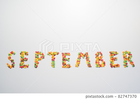 The inscription September on a white background. Confectionery sprinkles in the form of multi-colored maple leaves 82747370