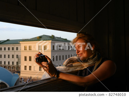 Portrait of a female photographer at work in the embrasure of a medieval tower at sunset 82748010