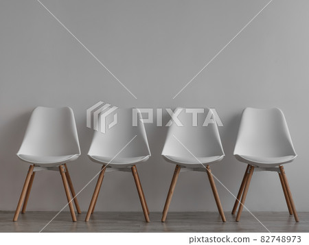 Four vacant white chairs on gray wall background in office or living room 82748973
