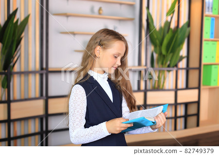 Portrait of a girl in a school uniform with a book in her hands. The child reads a textbook. Preparing a schoolgirl for a school lesson or exam 82749379