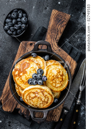 Pancakes with fresh blueberries and maple syrup in a pan. Black background. Top View Pancakes with fresh blueberries and maple syrup in a pan. Black background. Top View 82749583